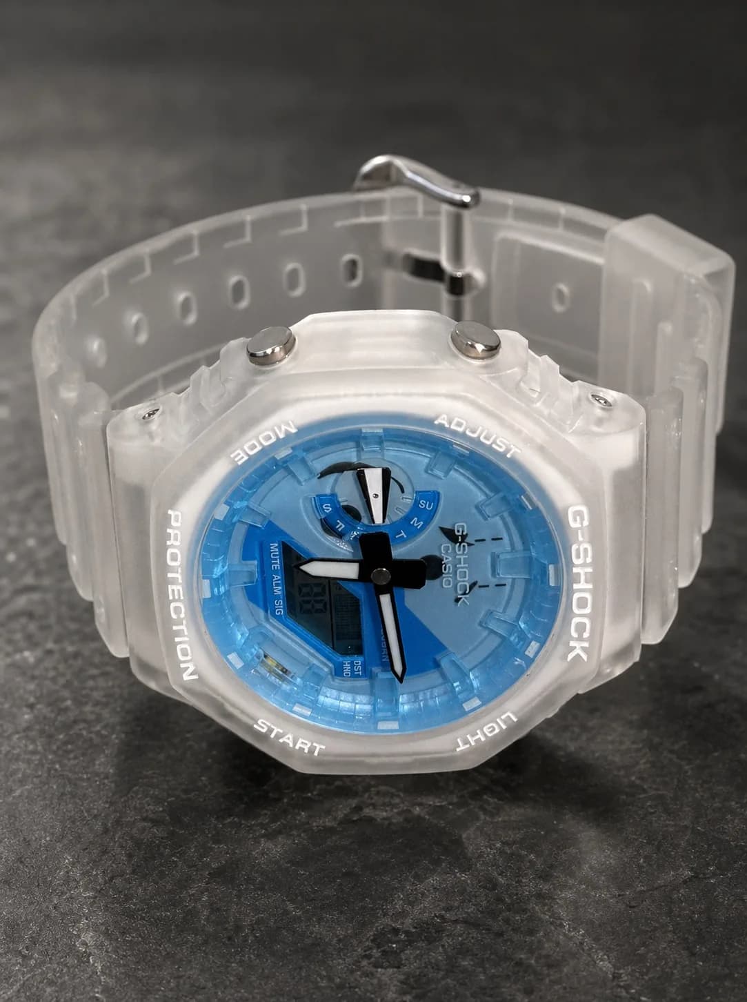 La même montre de trois quarts, posée sur ardoise : épaisseur du boîtier translucide et attache du bracelet.