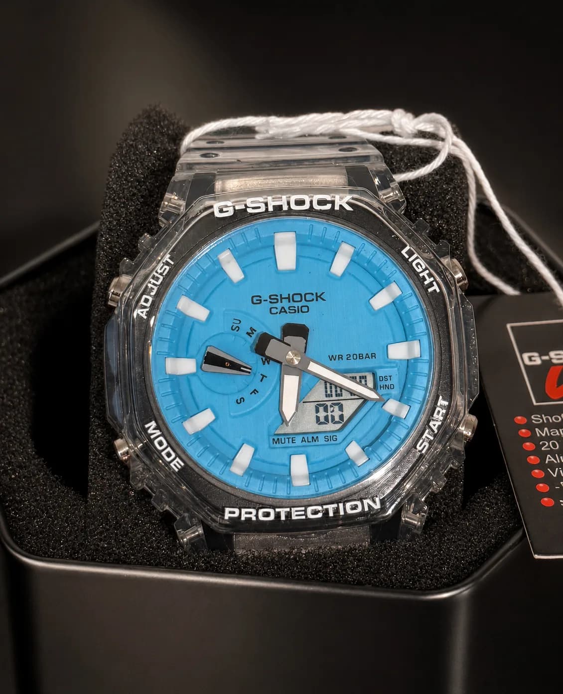 GA-2100BM-7A2ER de face dans sa boîte, étiquette d’origine attachée : cadran bleu vif, index blancs, boîtier transparent.
