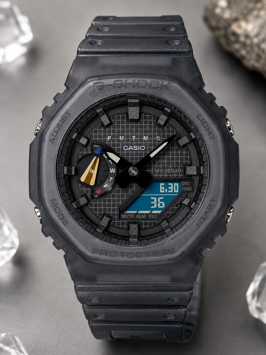 GA-2100FT-8AJR, de face : boîtier en résine translucide gris fumé, cadran gris à trame quadrillée, logo FUTUR en relief à midi, afficheur digital bleu.